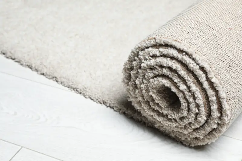 Rolled fuzzy carpet on wooden background, closeup. 